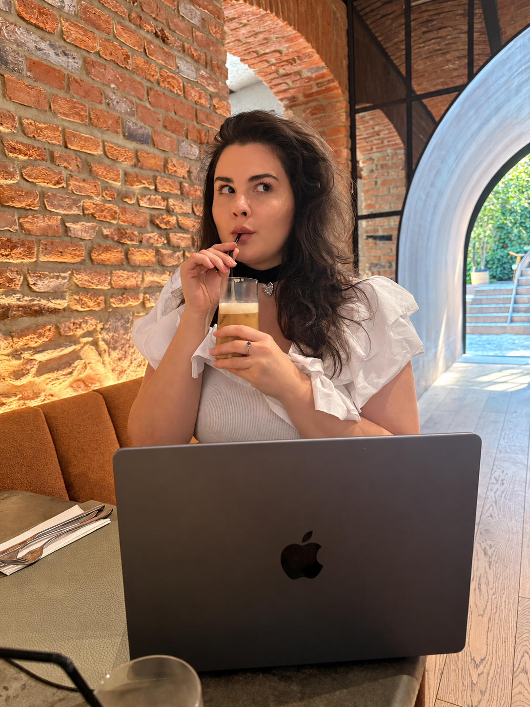 Andreea Chiș bea o cafea cu paie, cu laptopul deschis în față